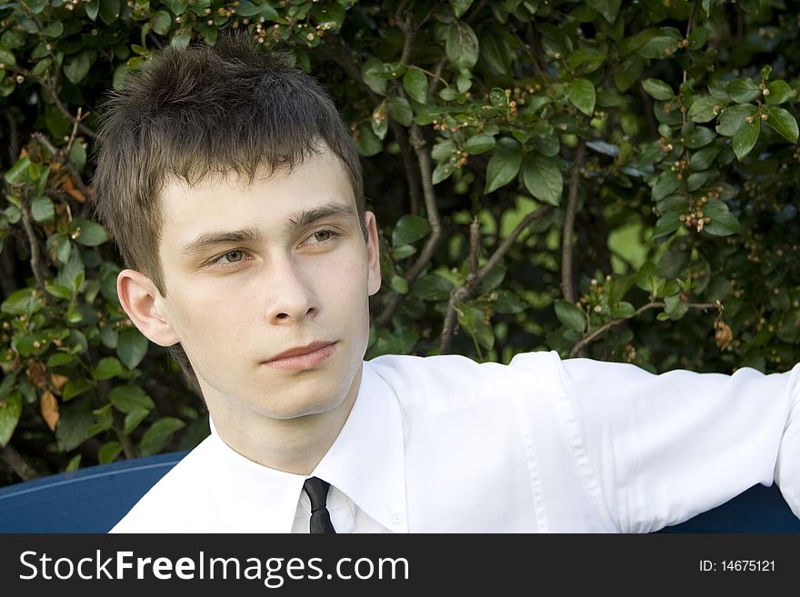 Teenager in a park sitting on a bench in a white shirt and tie, looking away. Teenager in a park sitting on a bench in a white shirt and tie, looking away