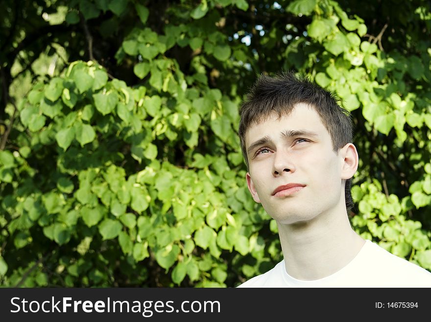 Teenager in a park in a white shirt against the green leaves of the tree. Teenager in a park in a white shirt against the green leaves of the tree