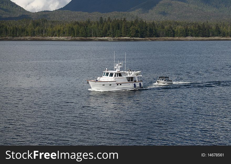 A small yacht cruises the calm waters near Bellingham, Washington USA while towing a smaller boat. A small yacht cruises the calm waters near Bellingham, Washington USA while towing a smaller boat.