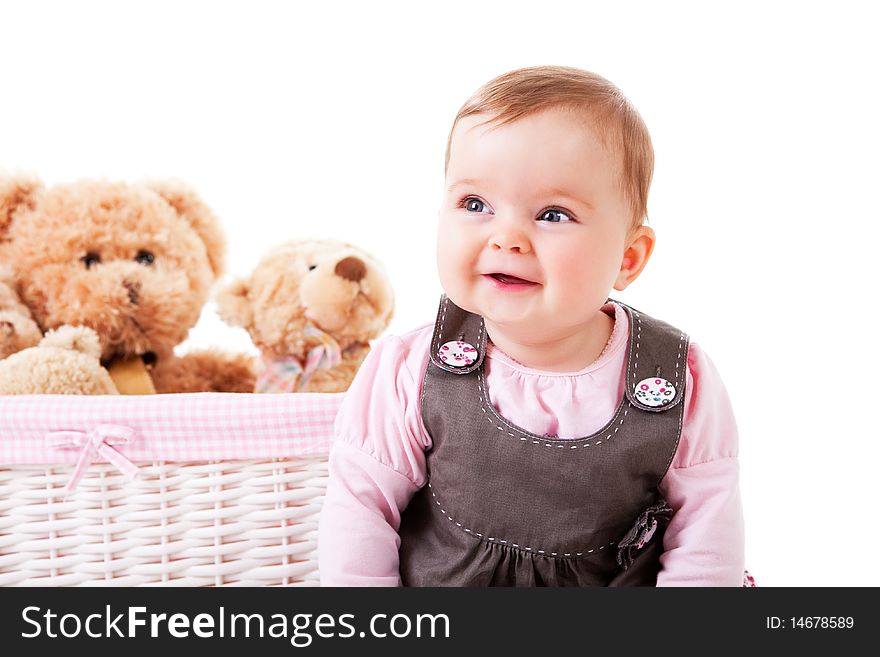 A baby girl is sitting next to a basket of teddy bears and smiling. Horizontal shot. A baby girl is sitting next to a basket of teddy bears and smiling. Horizontal shot.