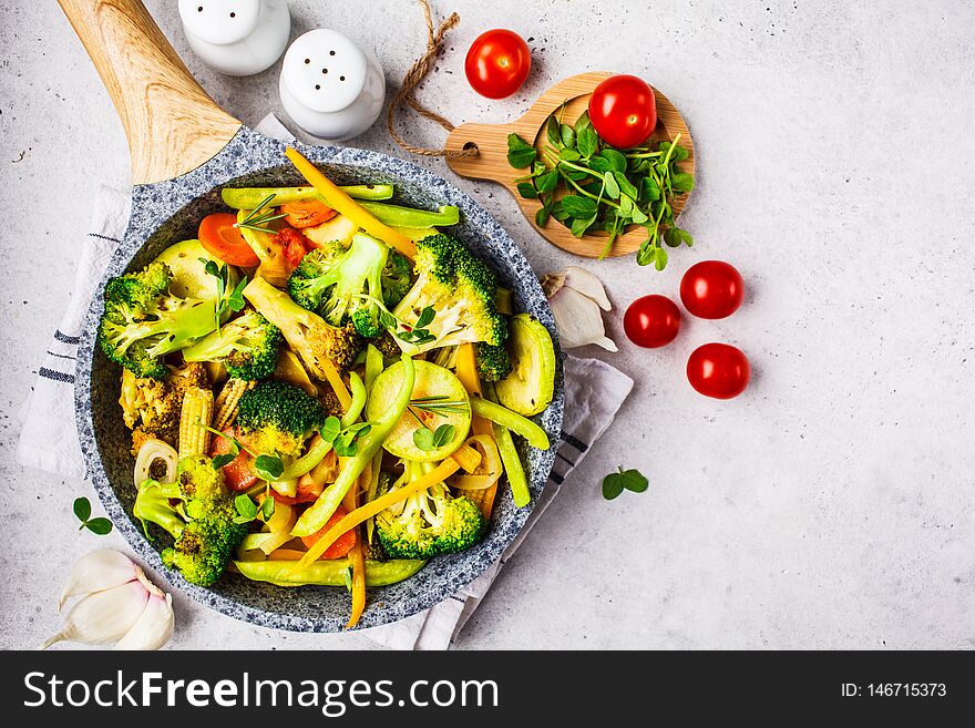 Fried broccoli, peppers, corn, zucchini and tomatoes in pan on a white background