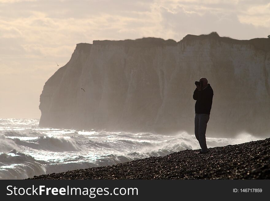Man photographing stormy seas near sheer cliffs