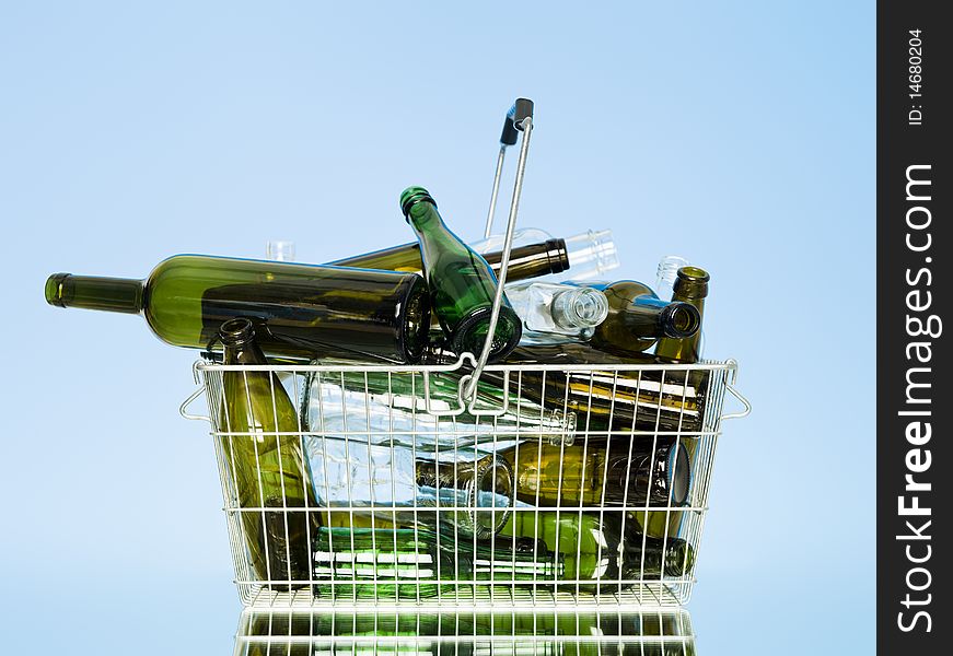 Empty glass bottles in a wastebasket on blue background