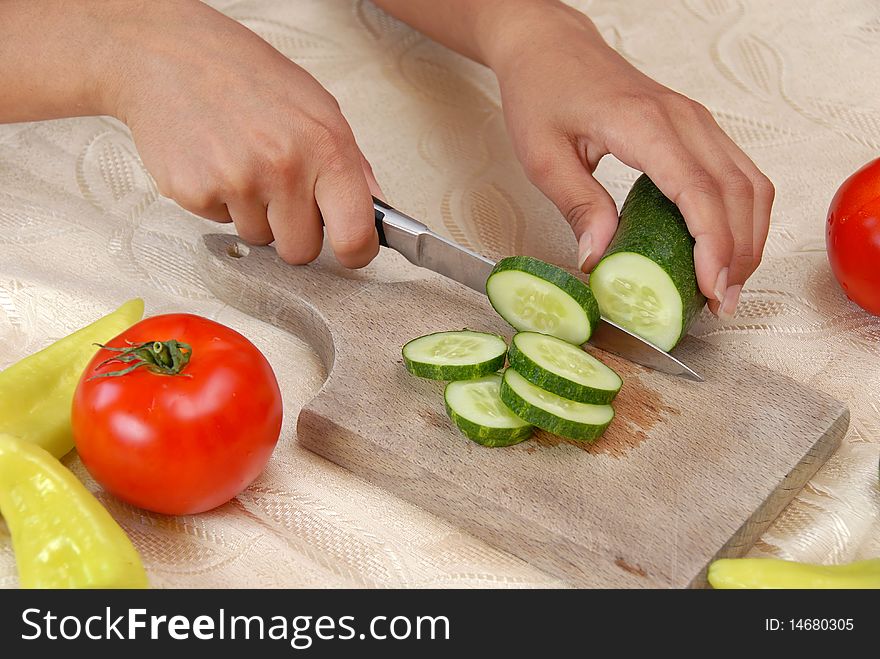 Female hands cutting cucumber for vegetable salad closeup on board. Female hands cutting cucumber for vegetable salad closeup on board