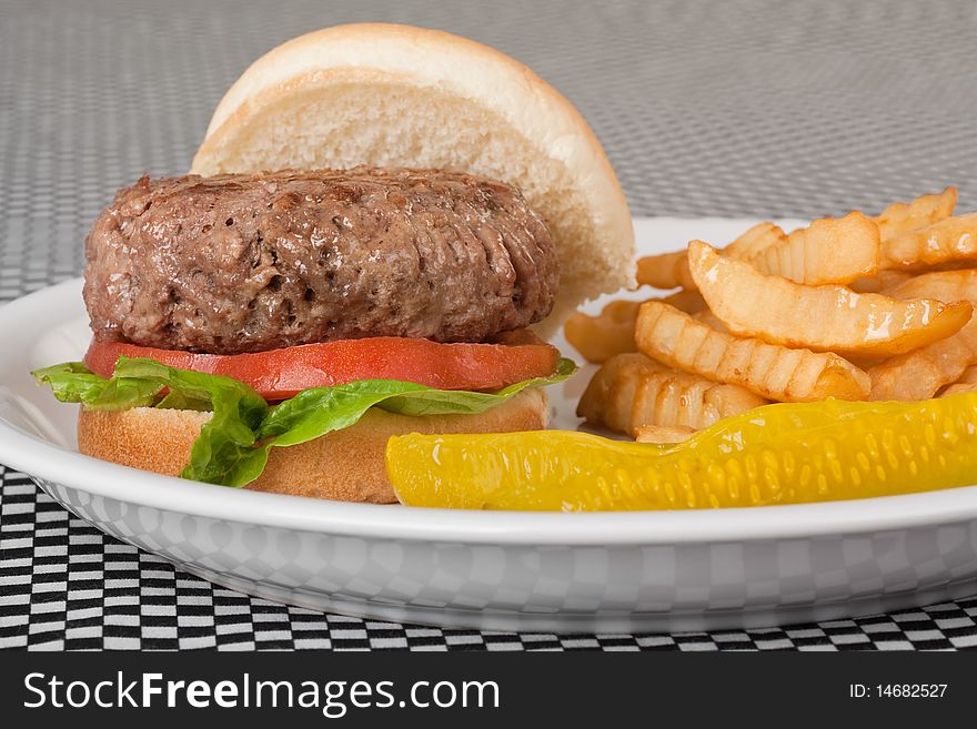 Closeup of a hamburger with tomato and lettuce on a bun along with french fries and pickle. Closeup of a hamburger with tomato and lettuce on a bun along with french fries and pickle