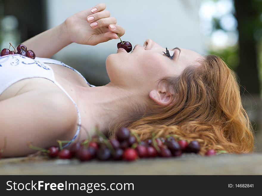 Red-haired beauty in a summer sarafan eating cherries
