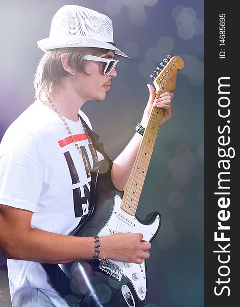 A young guitarist holding his guitar and performing over the stage background. A young guitarist holding his guitar and performing over the stage background