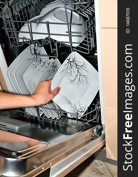 Hand takes a plate from the open dishwasher. Hand takes a plate from the open dishwasher