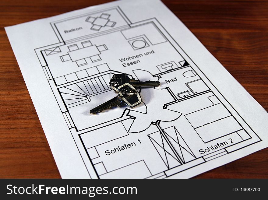 On a wooden table there is a ground plan of an apartment with keys on it. On a wooden table there is a ground plan of an apartment with keys on it