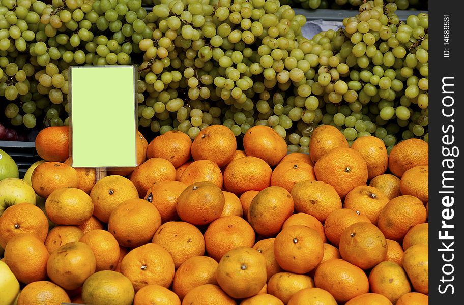 Green grapes and oranges with a sign at a market. Green grapes and oranges with a sign at a market