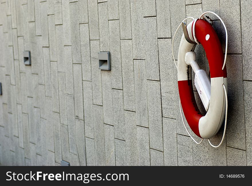 A red and white lifebuoy hanging on a stone wall