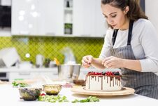 Confectioner Decorates With Berries A Biscuit Cake With White Cream And Chocolate. Cake Stands On A Wooden Stand On A Stock Photography