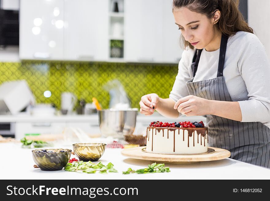 Confectioner Decorates With Berries A Biscuit Cake With White Cream And Chocolate. Cake Stands On A Wooden Stand On A