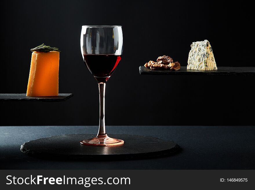Red wine in crystal glass beside pieces of cheese and walnut on black background.