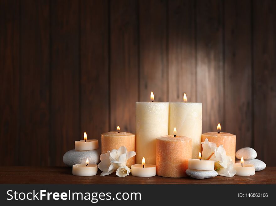 Beautiful composition with candles, flowers and stones on table against wooden background. Space for text