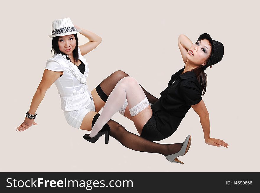 Two young pretty Asian woman in shorts and stockings, sitting on the floor
one in white, one in black holding there hats, on light beige Background. Two young pretty Asian woman in shorts and stockings, sitting on the floor
one in white, one in black holding there hats, on light beige Background.
