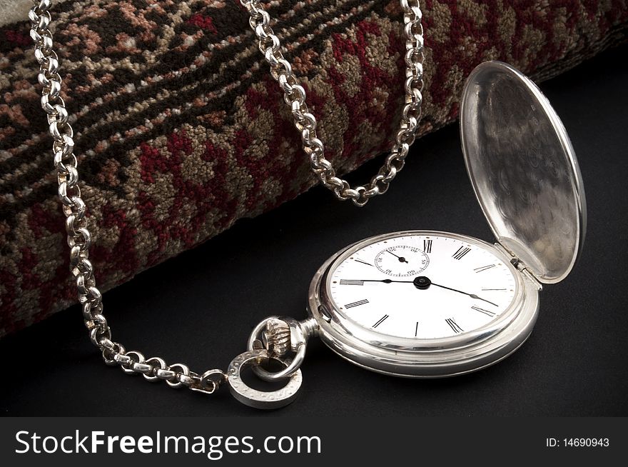 Elegant silver pocket watch over a rolled carpet