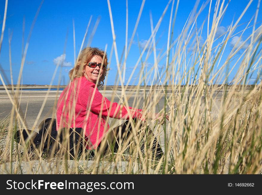 Woman sitting in the sand dunes on the beach with blue sky