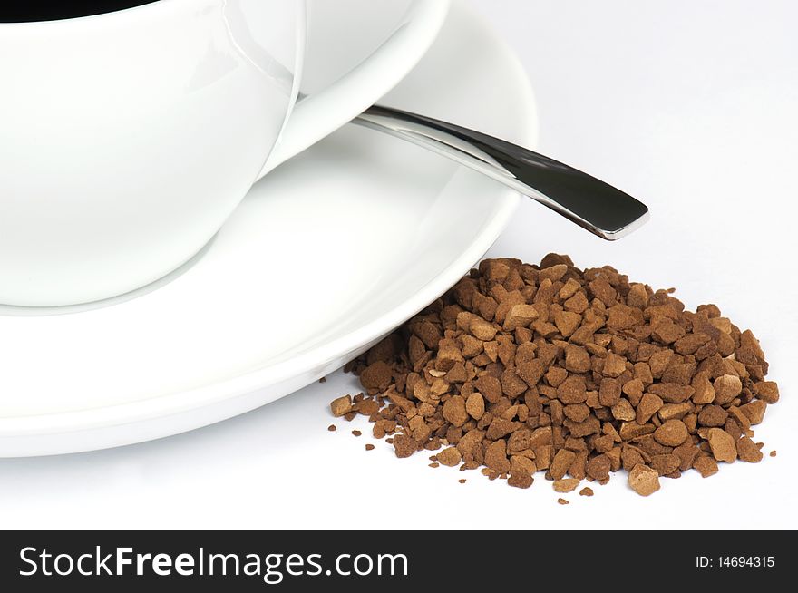 A Small Pile Of Instant Coffee Granules Next To A Cup and Saucer With Spoon
