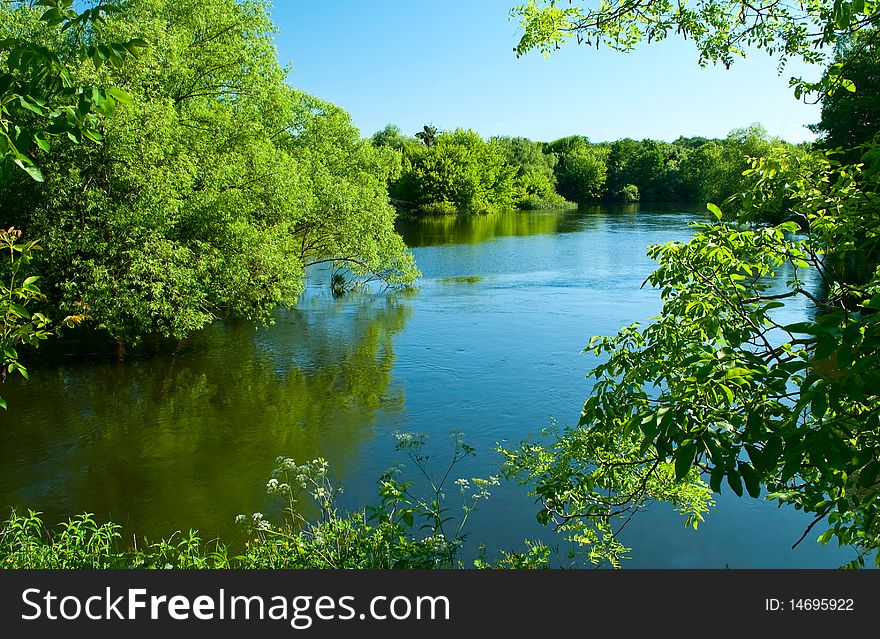 Shows the river, trees, grass and sky.