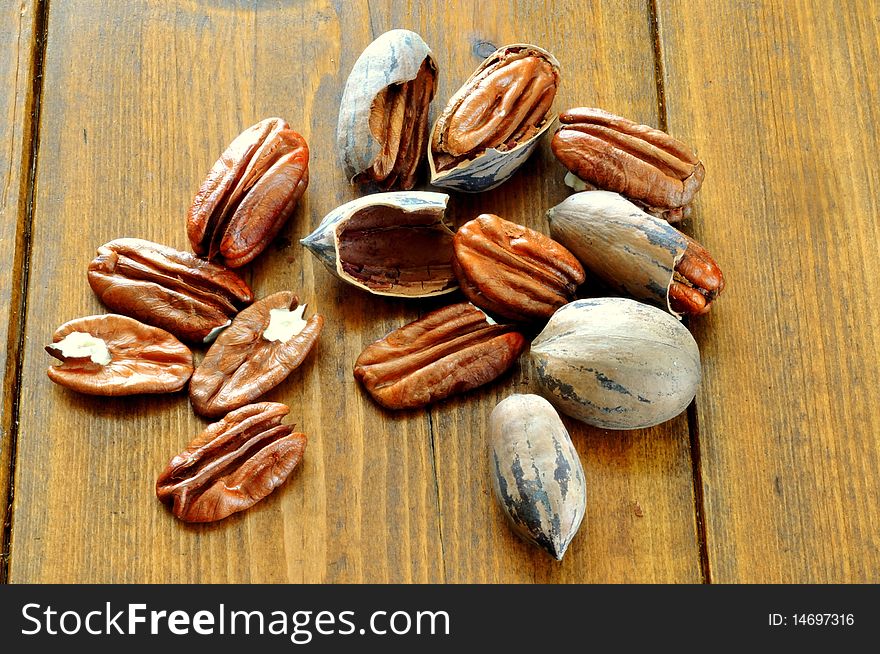 Pecans, whole and broken lie on the background of a wooden table. Pecans, whole and broken lie on the background of a wooden table
