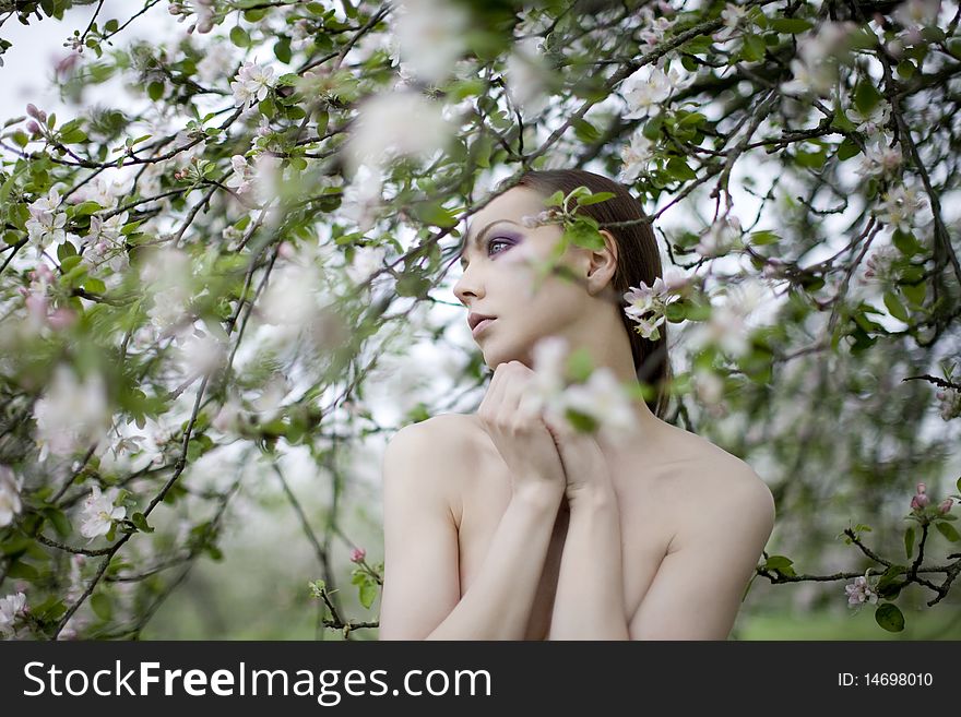 Young nude girl near blooming apple tree