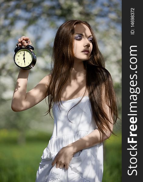 Young girl with an alarm clock in the meadow