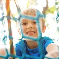 Happy Child Climbing On A Playground Ropes. Cheerful Little Boy Playing On Modern Playground. Smiling Kid Having Fun At Adventure Royalty Free Stock Photo