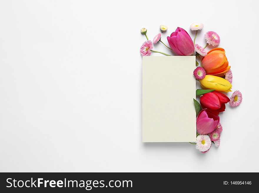 Beautiful composition with spring flowers and blank card on white background, top view.