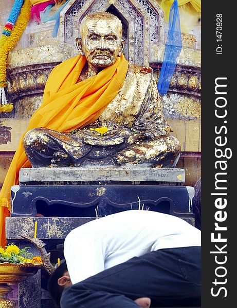 A Buddhist recites a prayer at the foot of a Buddha statue.