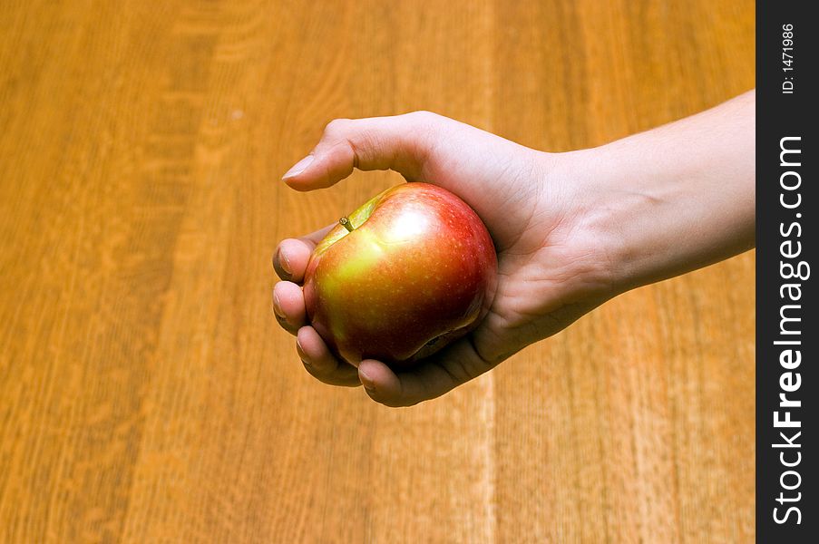 Boy's hand holding a macintosh apple with a oak table in the background. Boy's hand holding a macintosh apple with a oak table in the background
