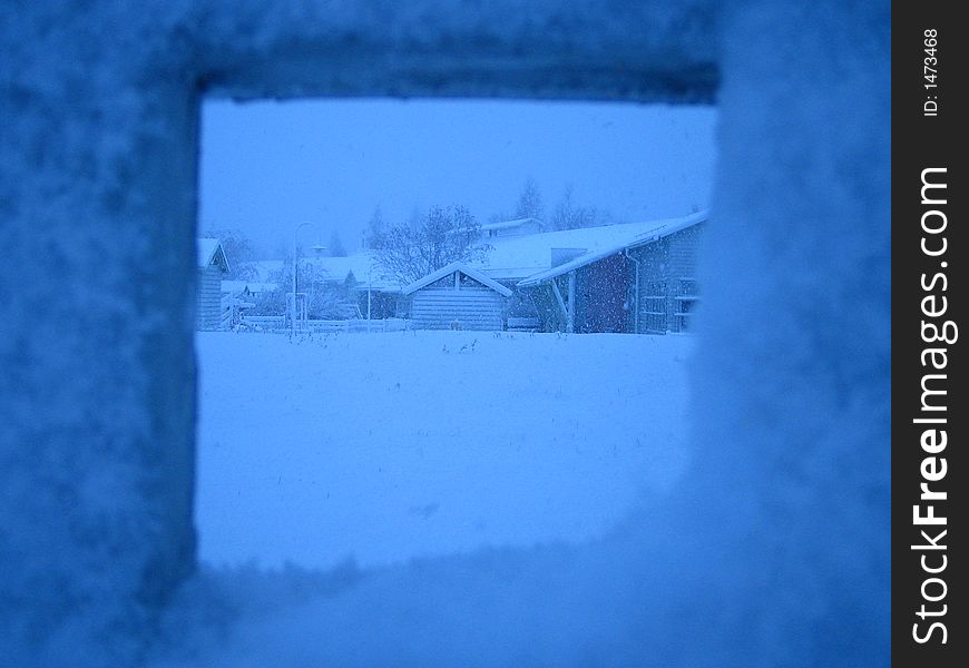 Picture exposes the view through a fence hole to the houses covered with the snow. Picture exposes the view through a fence hole to the houses covered with the snow.