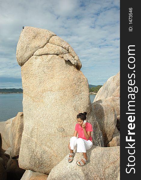 A beautifu young girl is talking on a mobile phone in front of some rocks on a tropical island resort while on vacation in Thailand. A beautifu young girl is talking on a mobile phone in front of some rocks on a tropical island resort while on vacation in Thailand.