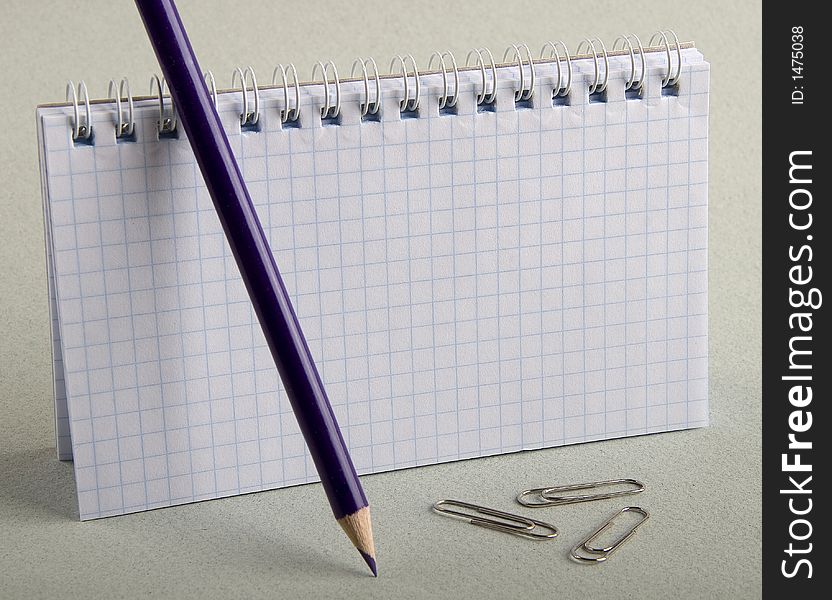 Notebook in a cell with a dark blue pencil and clips for a paper. Notebook in a cell with a dark blue pencil and clips for a paper