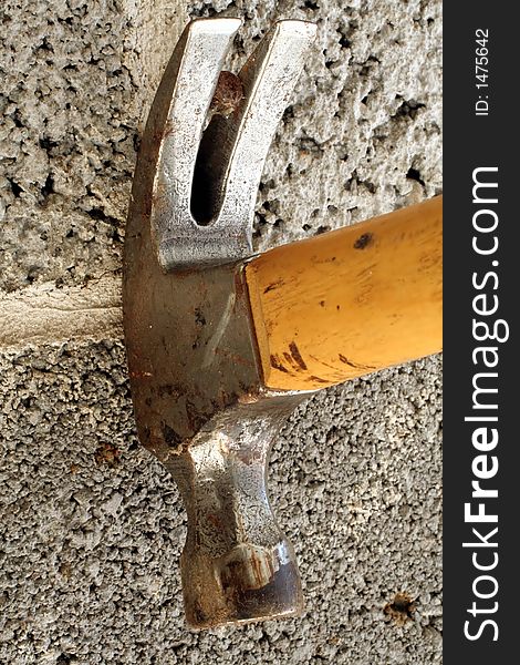 This is a close up image of a hammer pulling a nail out of a cinder block wall. This is a close up image of a hammer pulling a nail out of a cinder block wall.