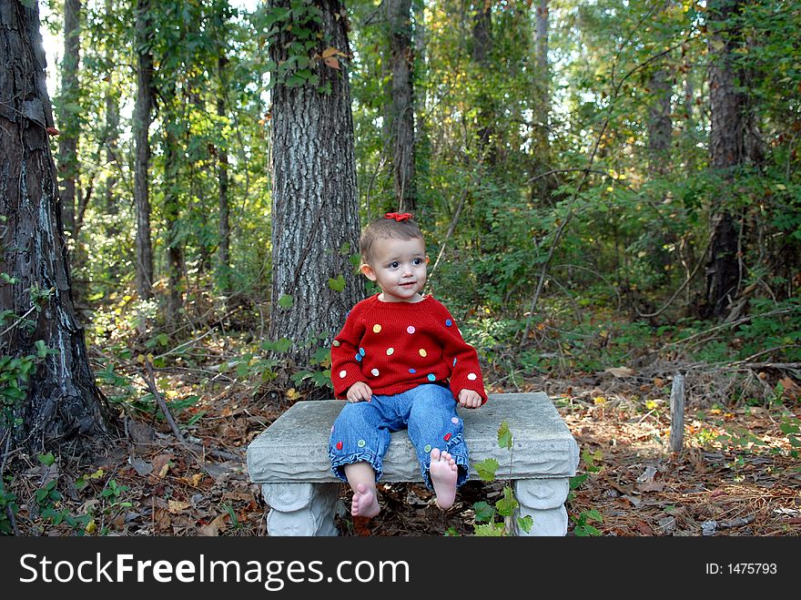 A baby girl sitting on a garden bench in an outdoor setting.  She's wearing a bright red sweater, blue jeans, a bow in her hair and is 

barefoot. A baby girl sitting on a garden bench in an outdoor setting.  She's wearing a bright red sweater, blue jeans, a bow in her hair and is 

barefoot.