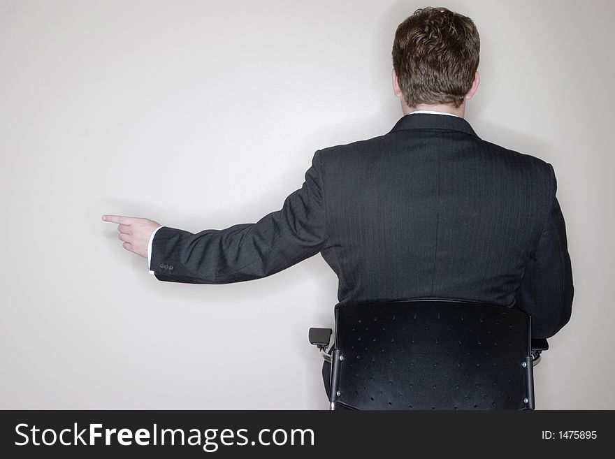 Businessman sitting and pointing in his office chair with a white background and a rear view