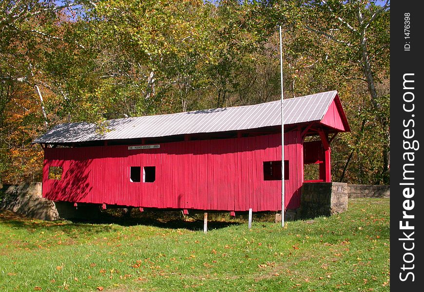 A red covered bridge shot from the side on a fall day. A red covered bridge shot from the side on a fall day
