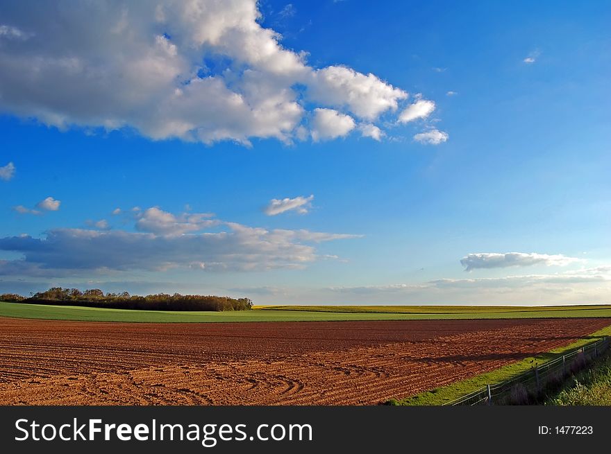 A field was just ploughed, with green corn fields and a woodland in the background. A field was just ploughed, with green corn fields and a woodland in the background.