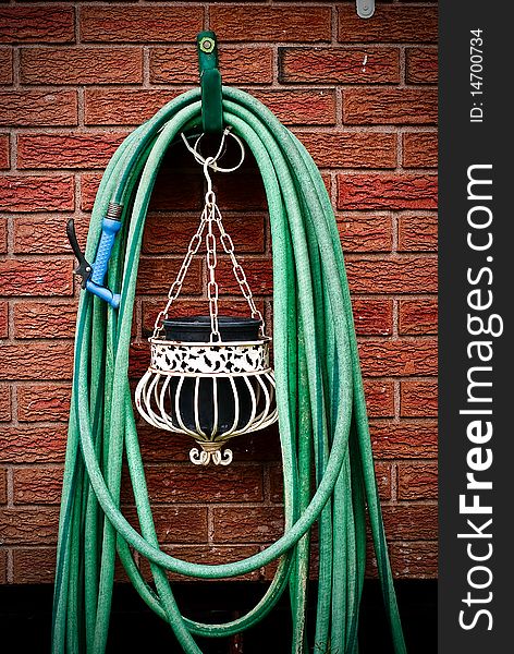 A common home garden hose coiled up and hanging on brick wall with hanging planter underneath. A common home garden hose coiled up and hanging on brick wall with hanging planter underneath.