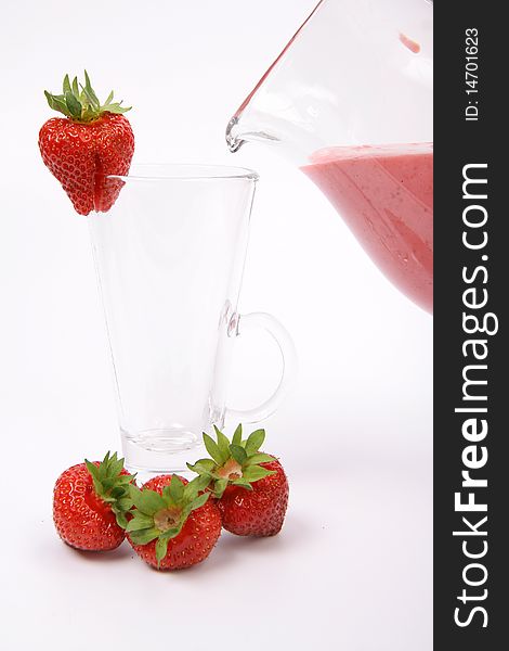 Strawberry shake being poured into a glass from a jug and some strawberries on white background