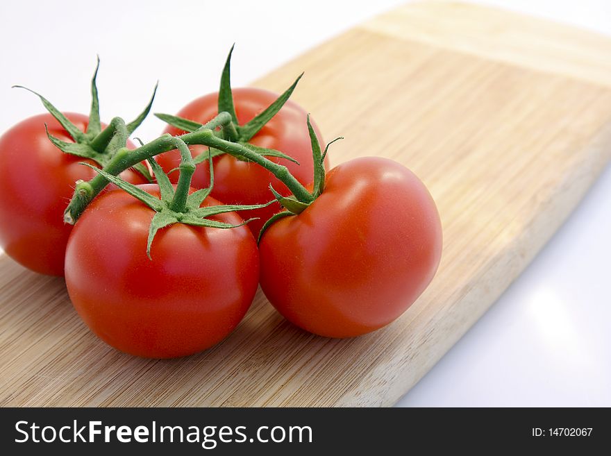 Four Red Tomatoes on a Wooden Cutting Board.