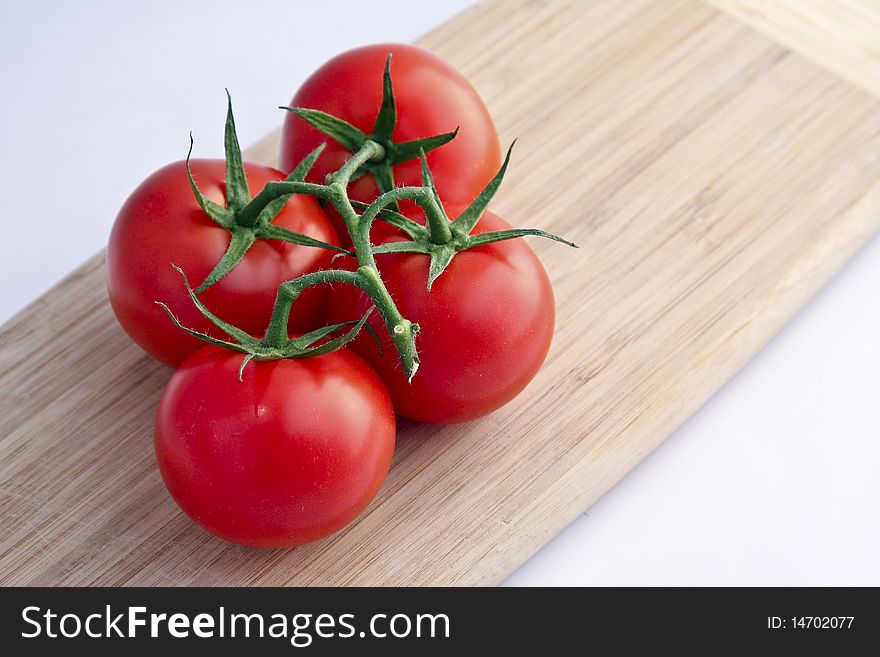 Four Red Tomatoes on a Wooden Cutting Board.