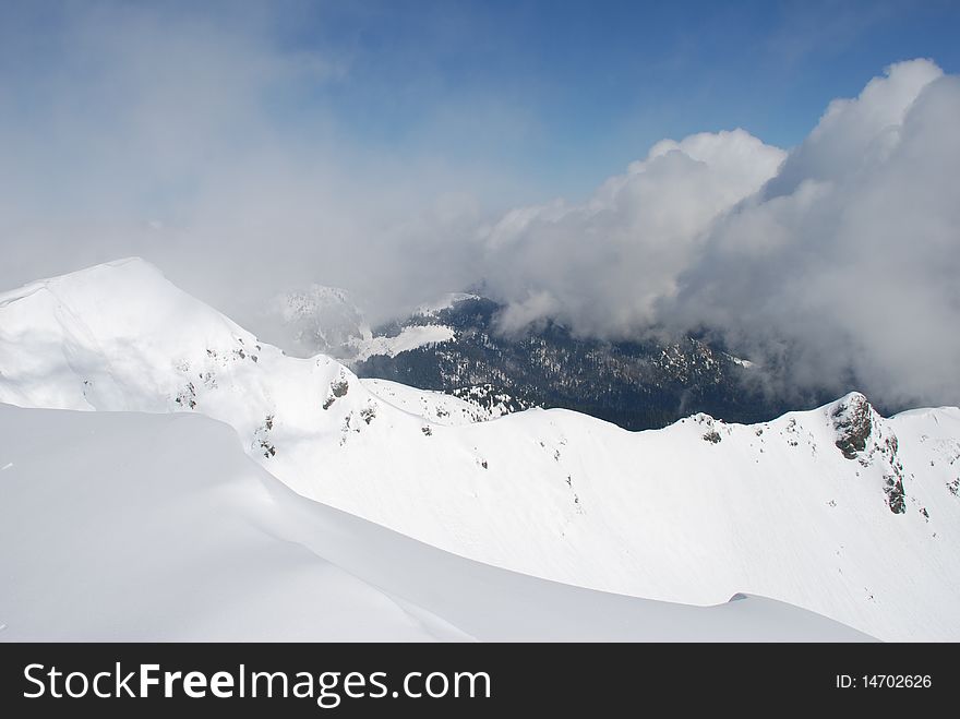A mountain winter slope in clouds in a landscape with white snow. A mountain winter slope in clouds in a landscape with white snow.