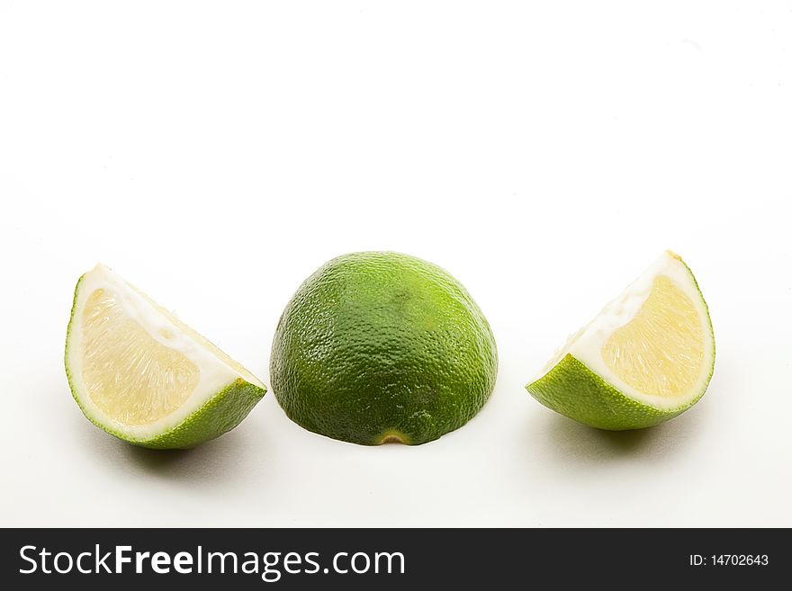 Two lime sections pulp on either side of a face down half with rind showing on white background. Two lime sections pulp on either side of a face down half with rind showing on white background.
