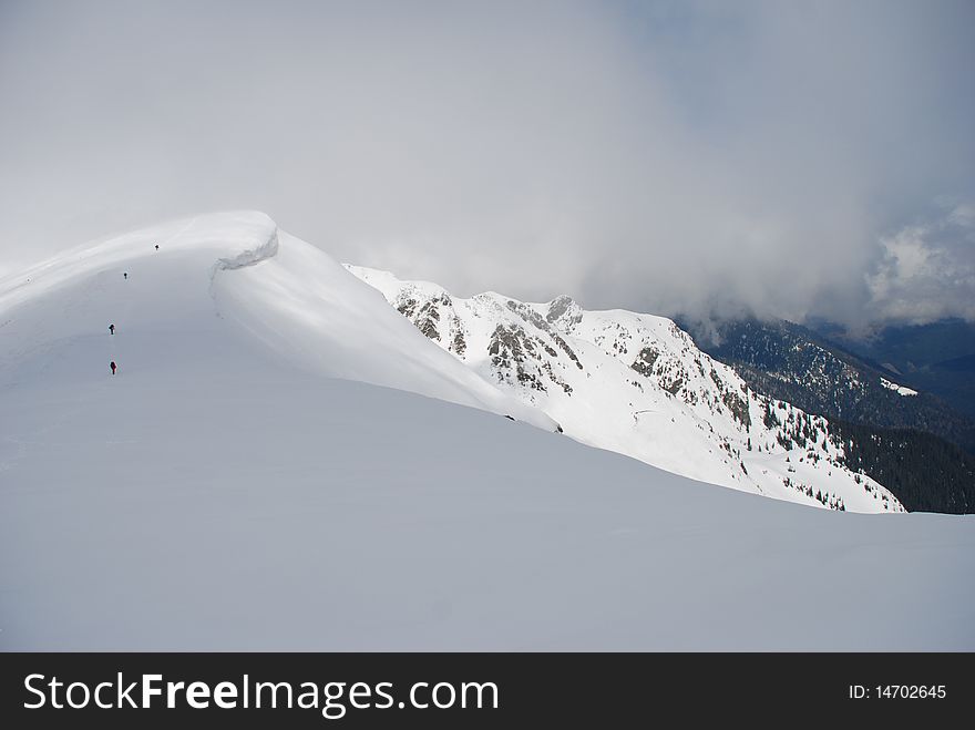 A mountain winter slope in clouds in a landscape with white snow and figures of tourists. A mountain winter slope in clouds in a landscape with white snow and figures of tourists.