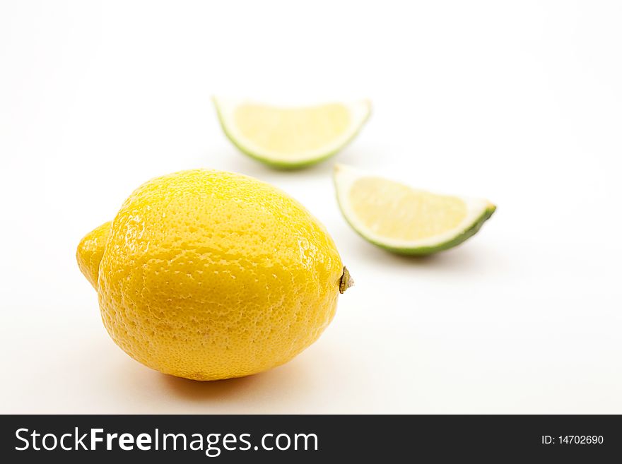 One whole lemon and two out of focus lime sections on white background. One whole lemon and two out of focus lime sections on white background.