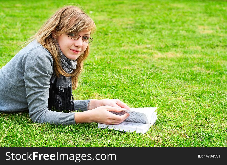 The girl lays on a green grass, and reads the book. The girl lays on a green grass, and reads the book