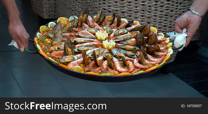 Two men holding a large dish of seafood paella