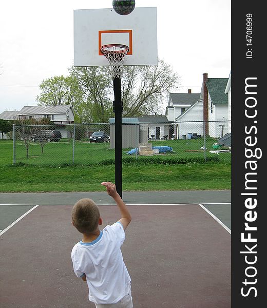 A young boy shoots hoops. He enjoys it and gets exercise. A young boy shoots hoops. He enjoys it and gets exercise.